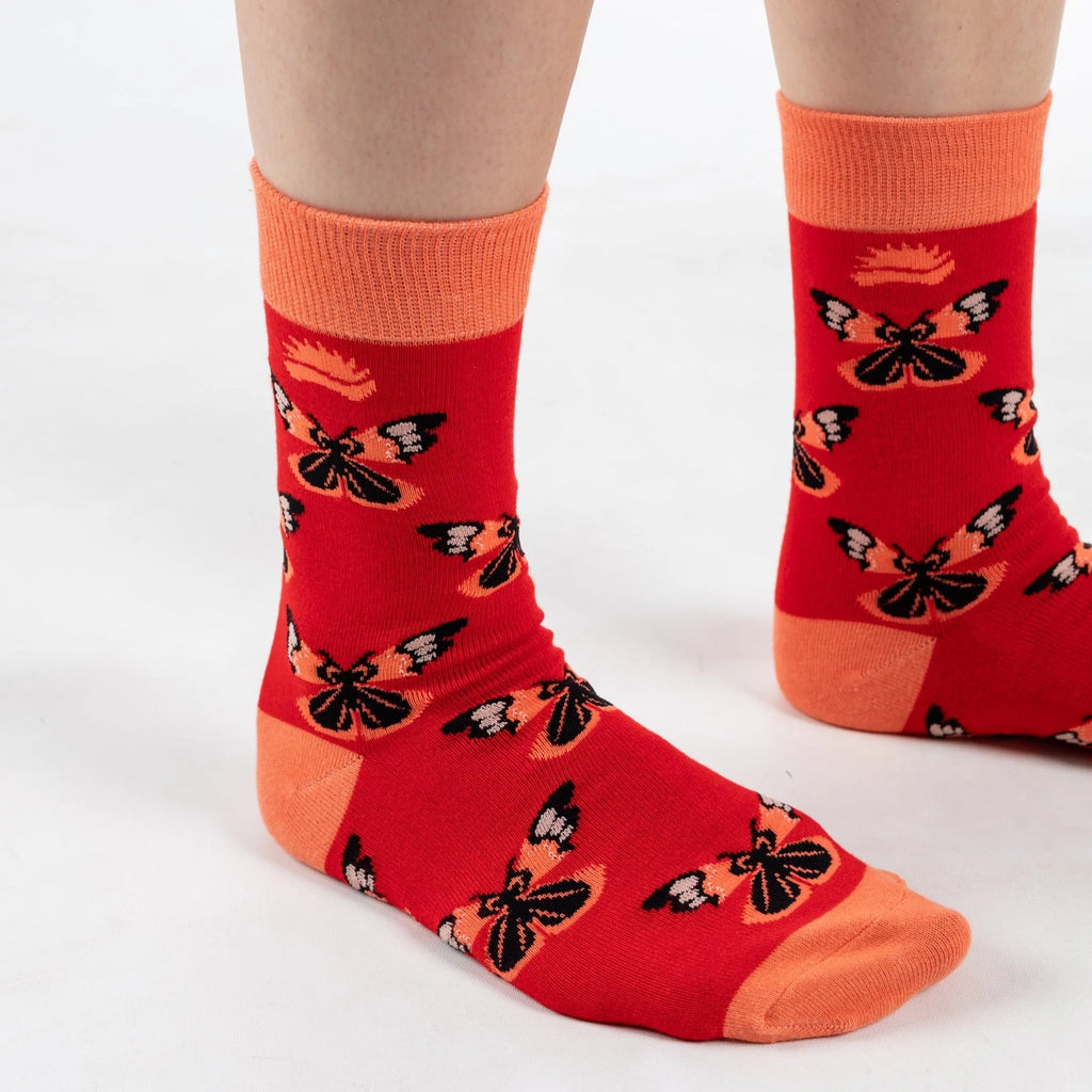 Front on view of model in super soft premium quality bamboo socks with an orange and red butterfly print on a red background with orange heel and toe