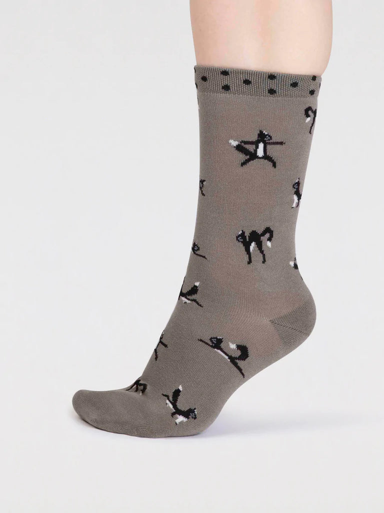 Side view of pea green bamboo and cotton socks with a black cat in yoga positions print and black spots around the cuff