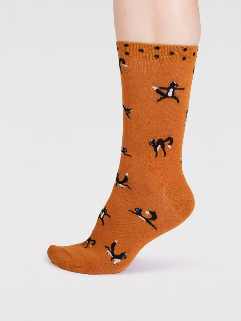 Side view of turmeric yellow bamboo and cotton socks with a black cat in yoga positions print and black spots around the cuff