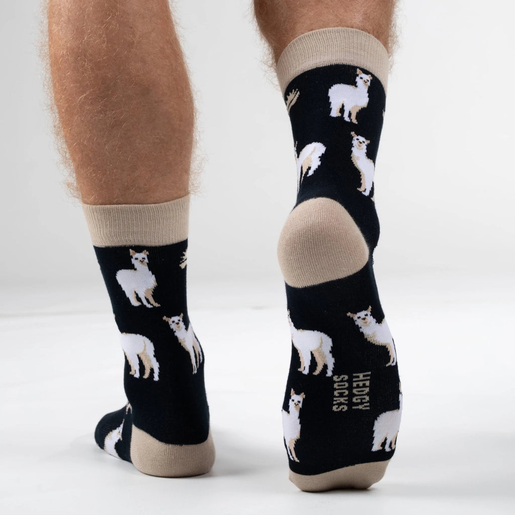 Back end view of model walking away in super soft premium quality bamboo socks with a beige and white Alpaca print on a black background and brand logo on sole of foot