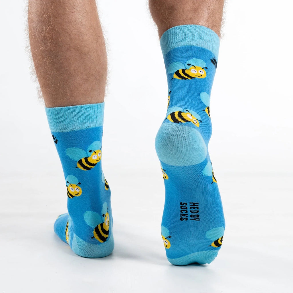 Back end view of model walking away in super soft premium quality bamboo socks featuring a yellow bee with blue wings design on a vibrant blue background