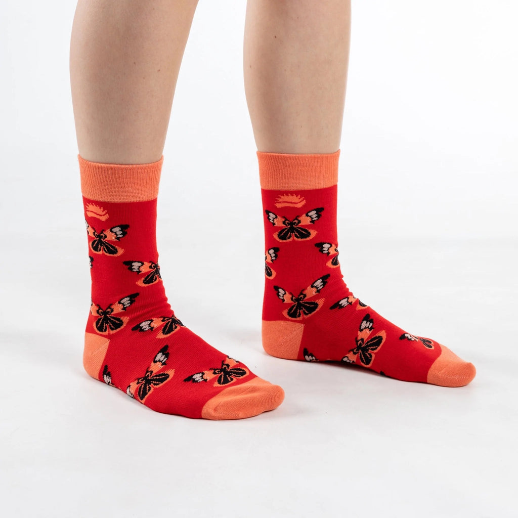 Front on view of model in super soft premium quality bamboo socks with an orange and red butterfly print on a red background with orange heel and toe